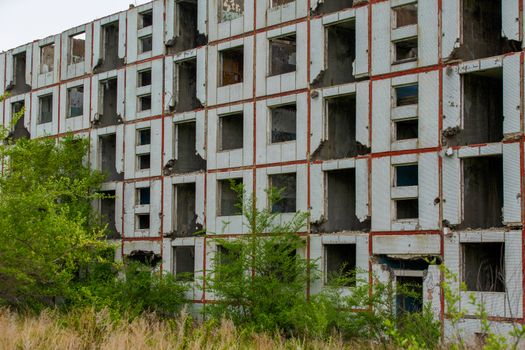 An abandoned multi-storey building stands in the middle of a green field.