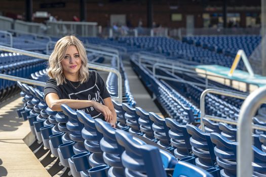A gorgeous blonde model poses outdoors near a baseball diamond before a game