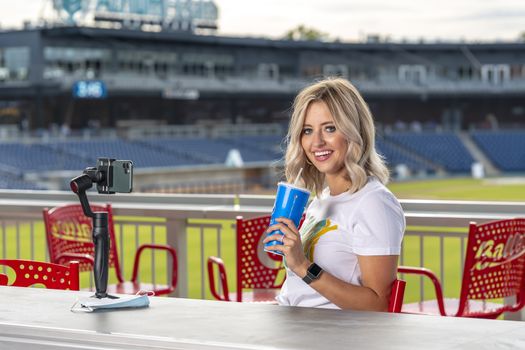 A gorgeous blonde model poses outdoors near a baseball diamond before a game