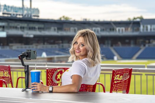 A gorgeous blonde model poses outdoors near a baseball diamond before a game