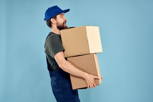Man in working uniform with boxes in hands delivery service blue background. High quality photo