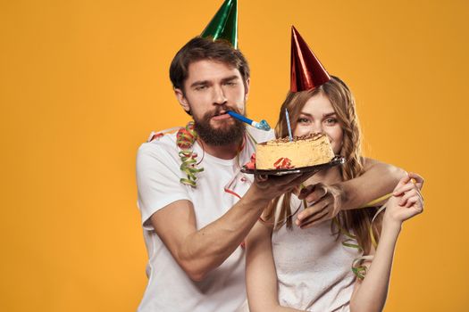 Happy man and woman with birthday cake birthday cap party yellow background. High quality photo
