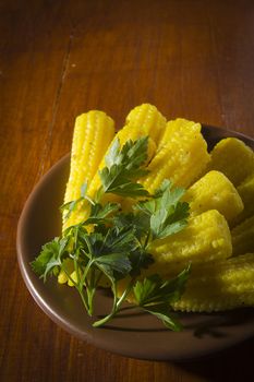 Pickled small cobs of corn in a plate on a wooden table