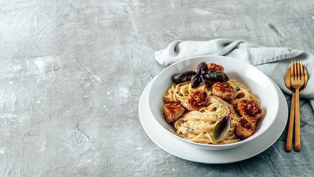 Zucchini Parmesan Meatballs with Pasta Carbonara in white plate over gray background. Close up view of creamy carbonara with copy space left