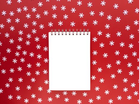 Blank sheet of notebook with scattered white snowflakes on red background. Educational concept. Simple flat lay with copy space. Stock photography.