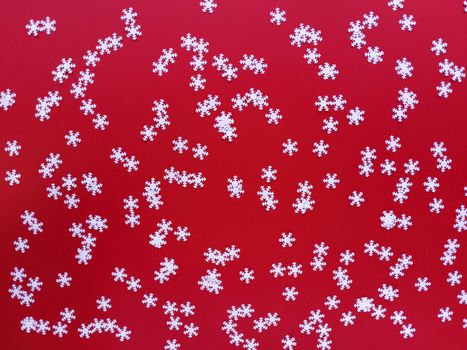 Scattered white snowflakes on red background. Simple festive flat lay. Stock photography.