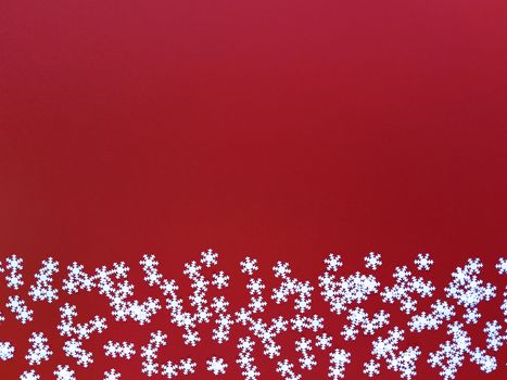 Scattered white snowflakes on red background. Simple flat lay with copy space. Stock photography.