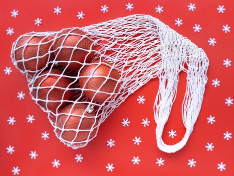 White string cotton eco bag with five christms tree balls on red background and scattered white snowflakes. Holiday simple flat lay. Ecology zero waste concept. Stock photography.