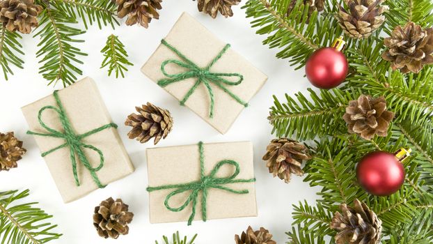 Holiday postcard with craft gift boxes, fir tree branches, cones and red christmas baubles on white background.