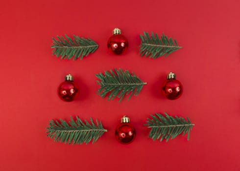 Christmas symmetry composition from toy baubles and fir tree branches on red background. Simple festive flat lay.