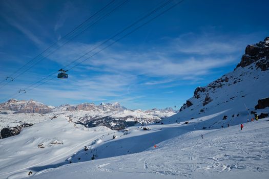 View of a ski resort piste with people skiing in Dolomites in Italy with cable car ski lift. Ski area Arabba. Arabba, Italy