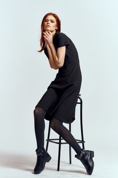 woman high chair indoors full length black dress red hair model boots. High quality photo