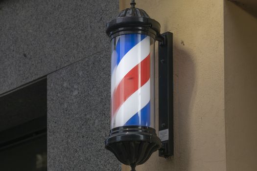 Classic barber pole with red, white and blue stripes, located on the facade of a building, on Calle Doce de Octubre, a commercial area of Madrid.