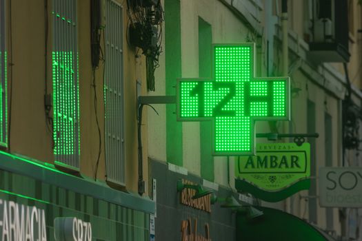 Madrid, Spain - May 19, 2020: The 12 H cross light sign located above the entrance area of one pharmacy in the Retiro district.