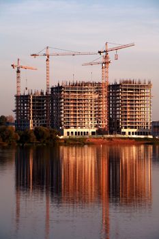 Building construction with cranes and reflection on river surface