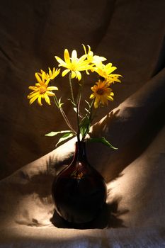 Nice yellow wildflowers in glass vase against canvas background