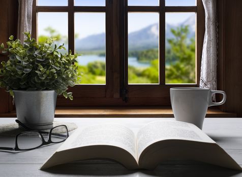 an open book on a wooden table in front of the panorama from the window