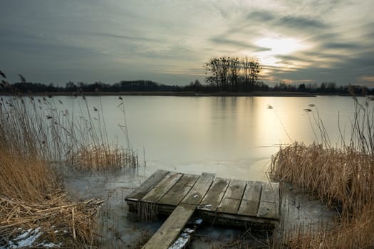A wooden platform in the reeds on the shore of a frozen lake, winter evening
