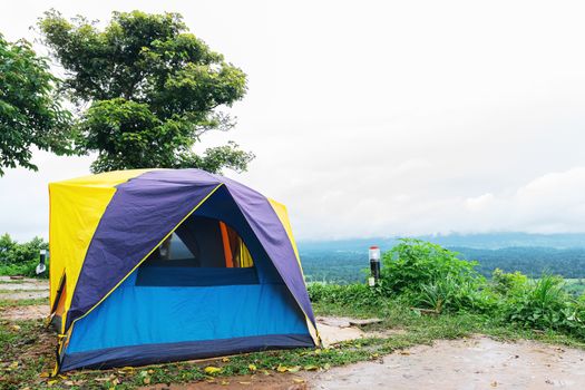 Camping tent that is set up at the highest point of a high mountain with a backdrop of sky and mountains.