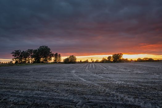 Ploughed field and dark clouds during sunset, summer view