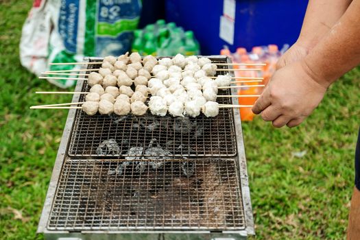 Close up of a man's hand grilling meatballs on a hot charcoal stove, Concepts for camping, vacations, and holidays.