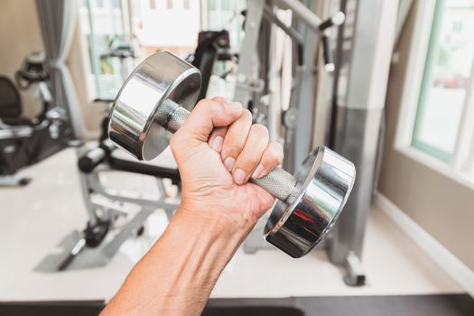 Closeup a man's hand holds a dumbbell with his left hand in the gym, Concept for exercise and health care.