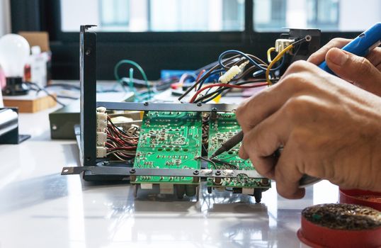 Electronic technician is soldering the electric wires to the motherboard of an electronic device.