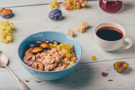 Healthy breakfast concept. Porridge with fresh plum, green grapes and cup of coffee. Ingredients over wooden background.