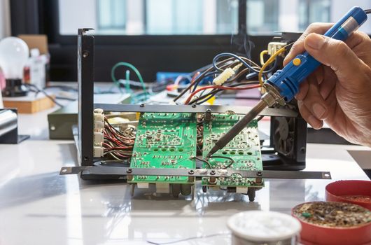 Electronic technician is soldering the electric wires to the motherboard of an electronic device.