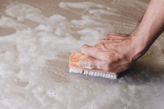 Men's hands are using a sponge cleaning the tile floor.