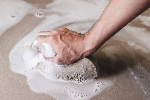 Men's hands are using a sponge cleaning the tile floor.