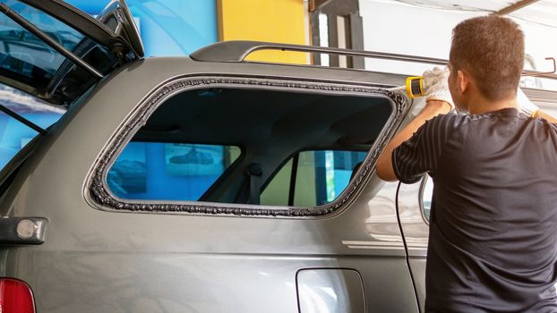 Technicians are using silicone to install the right rear glass of the car.