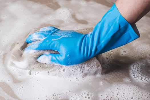 Hand of man wearing blue rubber gloves is using a sponge cleaning the tile floor.