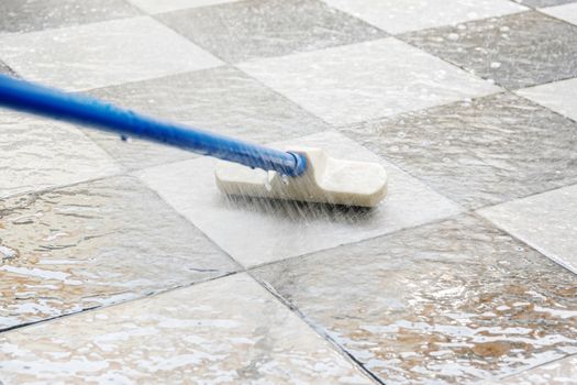 Cleaning the tile floor with floor scrubber brush and water.