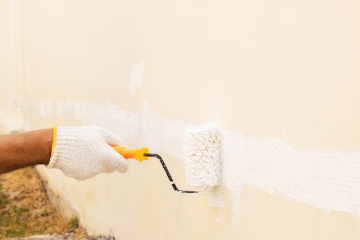 Closeup on hand wearing white cloth gloves, using a roller for painting white color on the concrete wall.