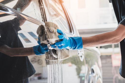 Car wash staff wearing blue rubber gloves using a sponge moistened with soap and water to clean the car.