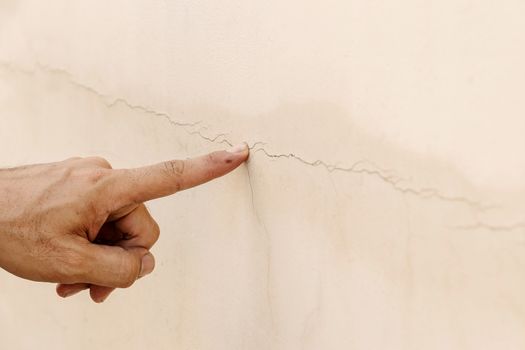 Close up of a man's hand pointing to a crack in the concrete wall.