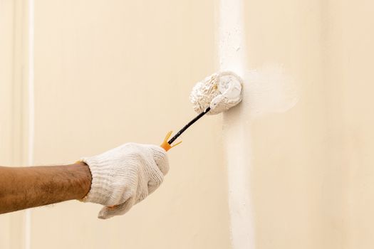 Closeup on hand wearing white cloth gloves, using a roller for painting white color on the concrete wall.