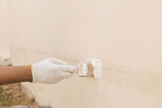 Close up of a hand with white cloth gloves that is being used to transform paint to seal the cracks on the concrete wall.