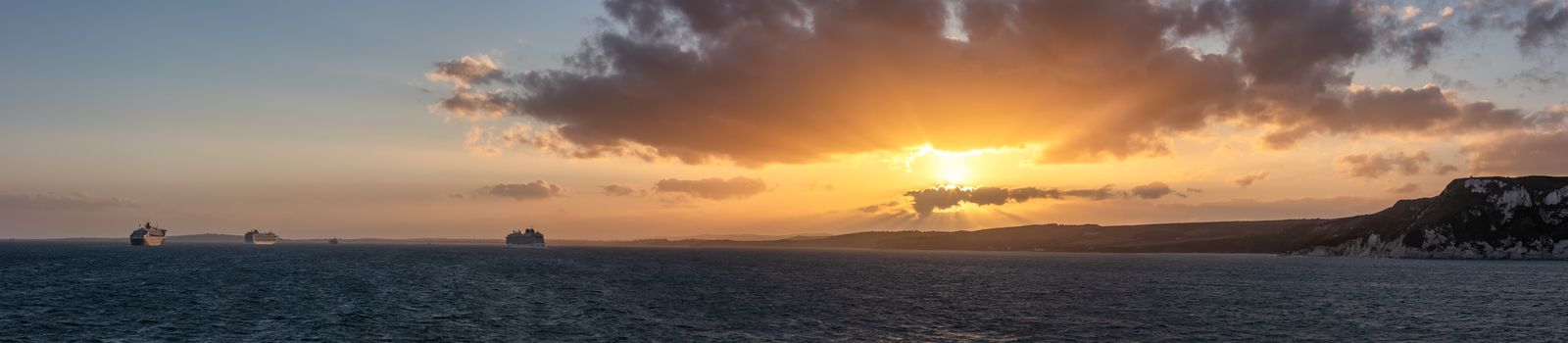 Beautiful sunset panorama of coast line in Weymouth Bay, UK. Gorgeous orange and yellow colors. Cruise ship anchored in the distance.