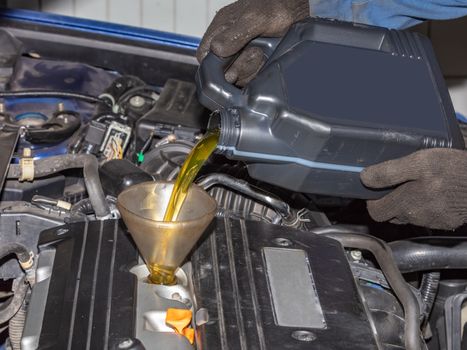Mechanic topping up the oil in a car pouring a pint of oil through a funnel into the engine, close up of his hands and the oil