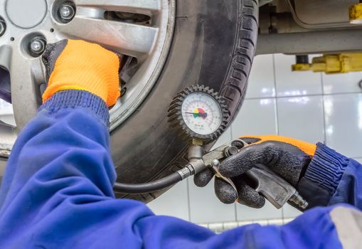 Closeup of mechanic wearing orange gloves and blue outfit at repair service station checking tyre pressure with gauge.