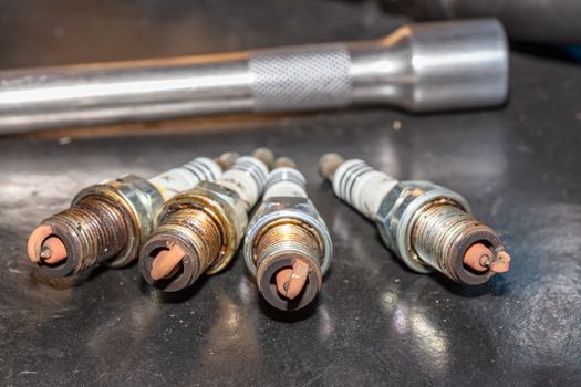 Shot of used spark plugs on a table with socket wrench blurred in the background. Car repair shop.