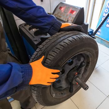 Mechanic working with wheel balancing machine at tire service, closeup. Mechanic wearing orange gloves and blue outfit.