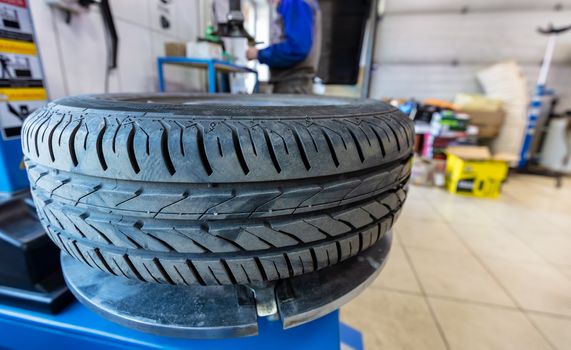 Close up shot of a tire on automatic tyre assembling and repair machine in garage. Unrecognizable mechanic standing behind it. Blurred background.