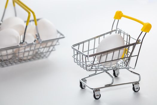 Fresh eggs in a shopping cart and a part of basket blurred in the background. Eggs in a basked out of focus. High angle view. Shopping, purchasing, and food delivery concept. White background. Close up shot. Isolated.
