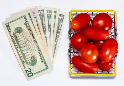 Shot of tomatoes in shopping basket isolated on white background with with various US dollar bills next to it. Ripe tasty red tomatos in shopping basket. Top view. Tomato trading concept. Online shopping concept. Copy space.