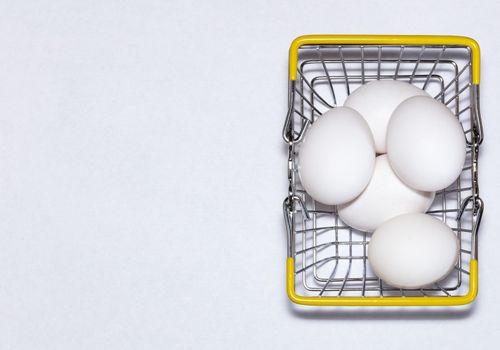 Fresh eggs in a shopping cart. Shopping, purchasing, and food delivery concept. White background. Close up shot. Isolated. Copy space.