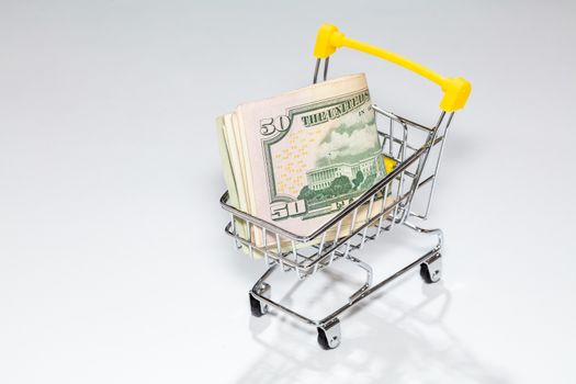High angle shot of a cart from the supermarket with money. US dollar on a white background. Concept of purchasing cost, a trip to the supermarket, costs of everyday shopping, expenses
