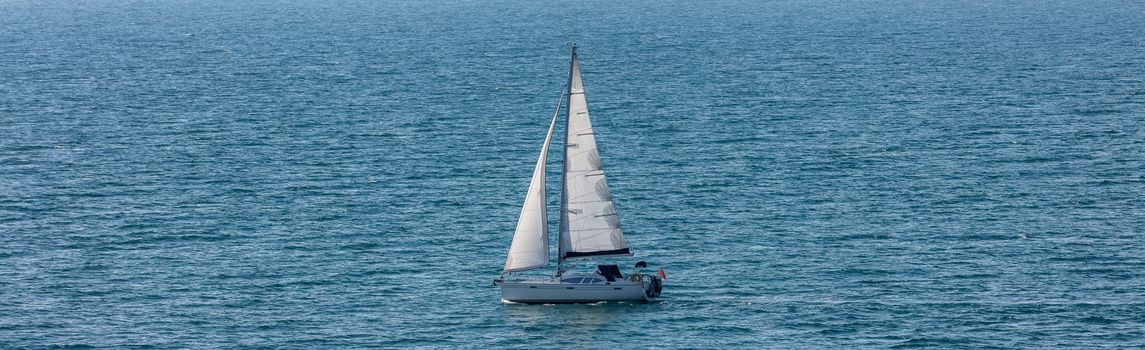 High angle shot of a white sailboat sailing in Weymouth Bay, UK. Sport and recreation concept.